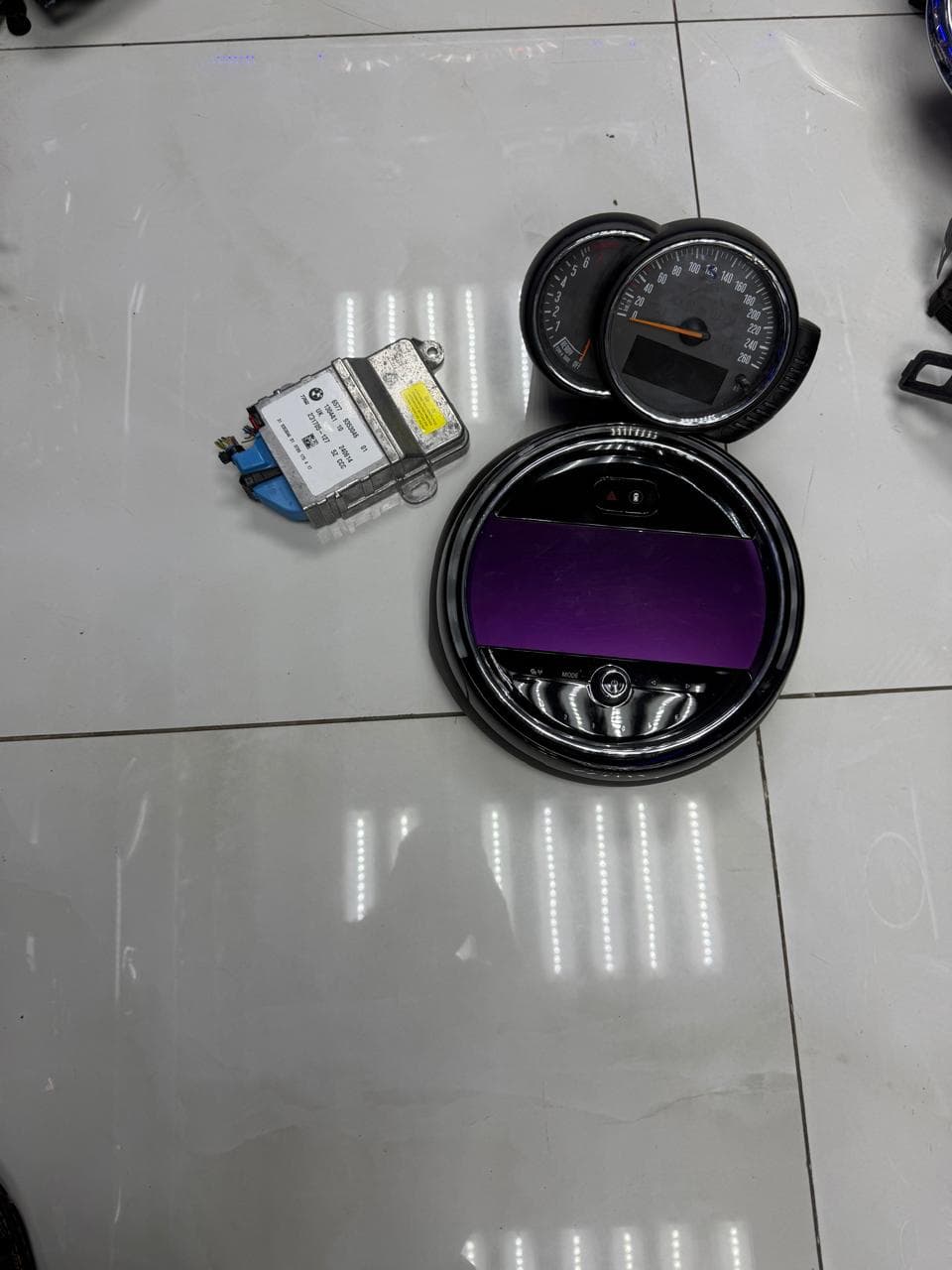 A MINI instrument cluster, centre display unit and control module laid out for inspection